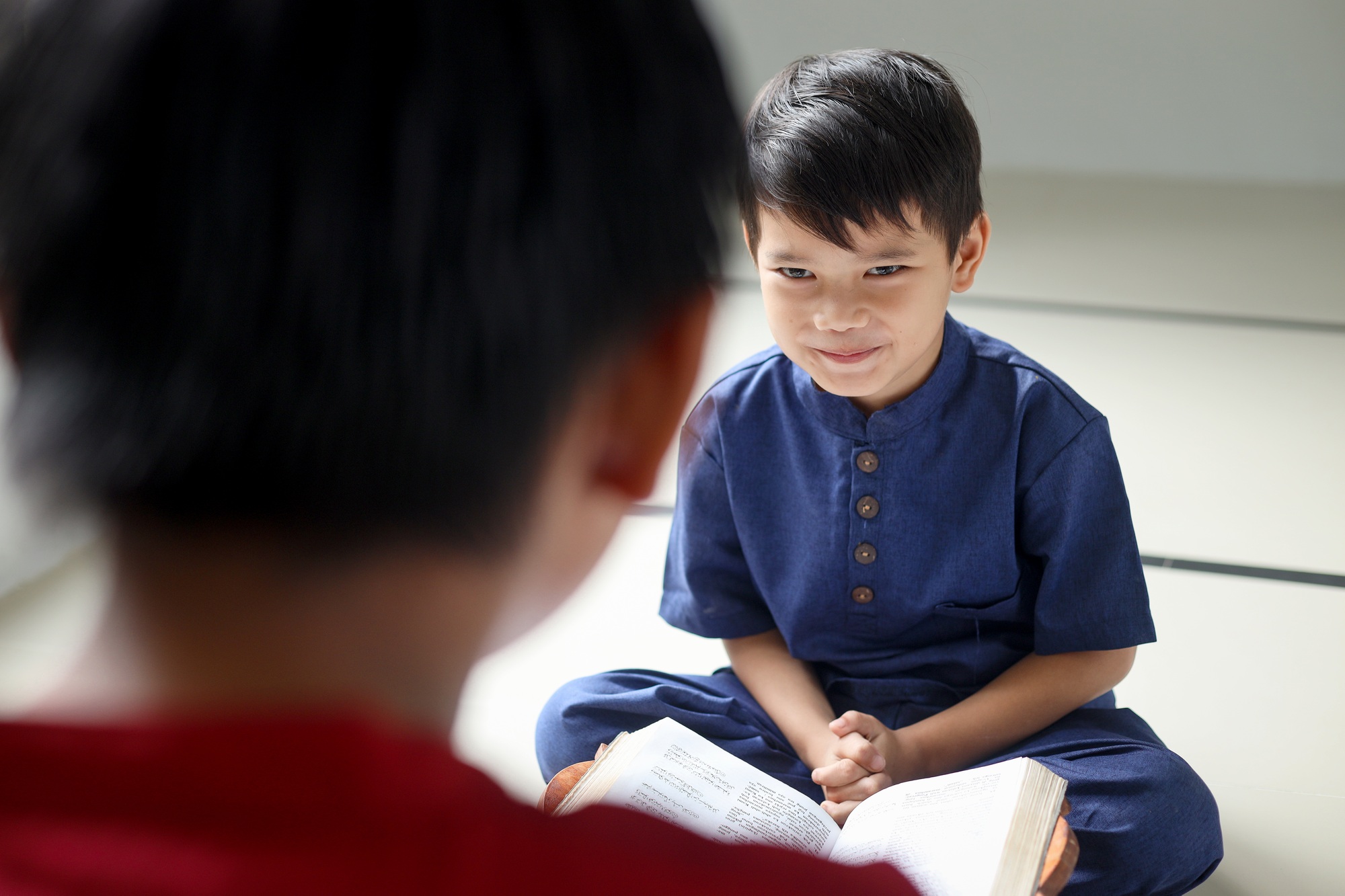 Rear view of Asian Muslim boy teaching brother how to read Quran inside the mosque